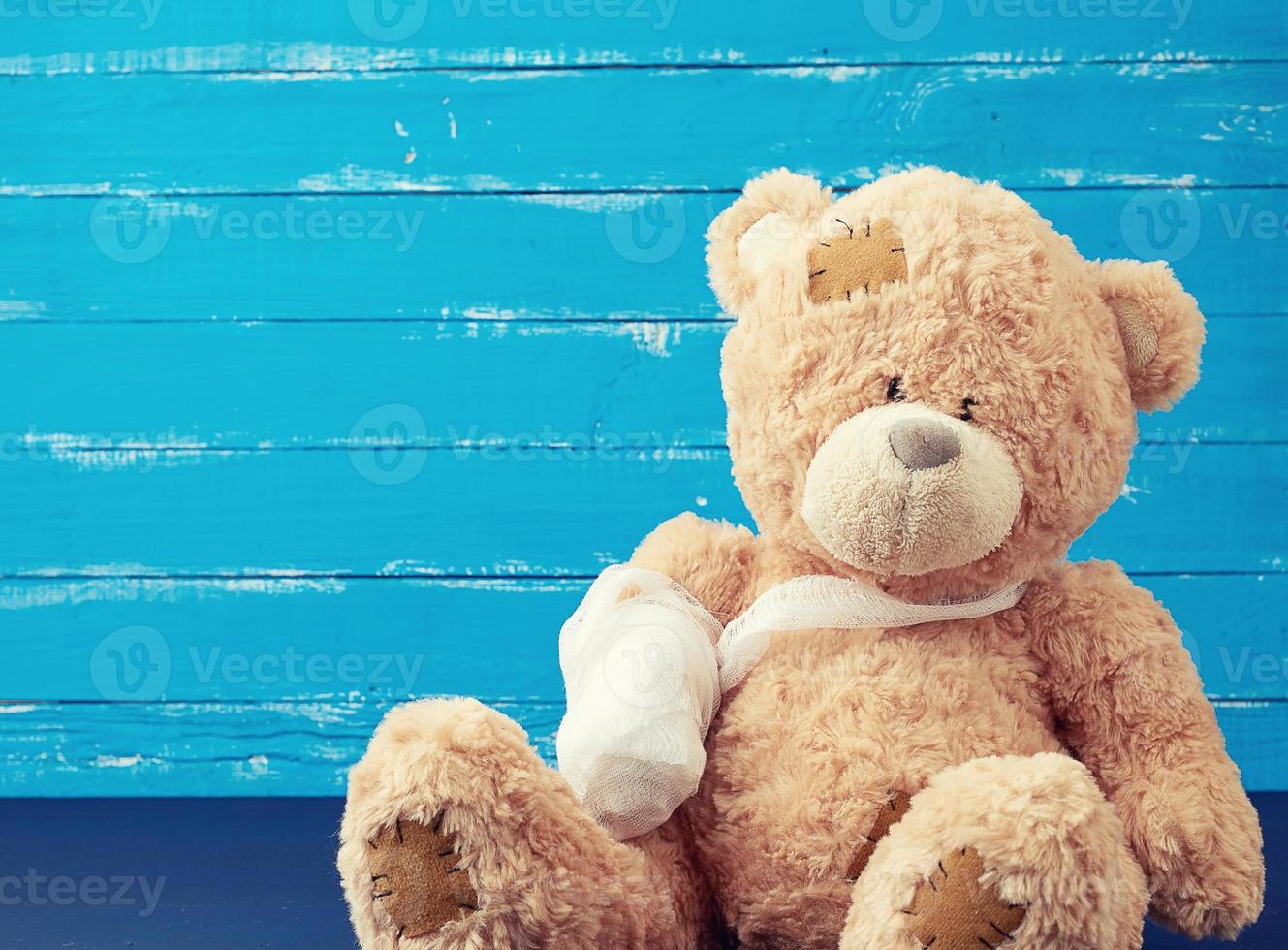 brown teddy bear with rewound white bandage paw on a blue wooden background photo