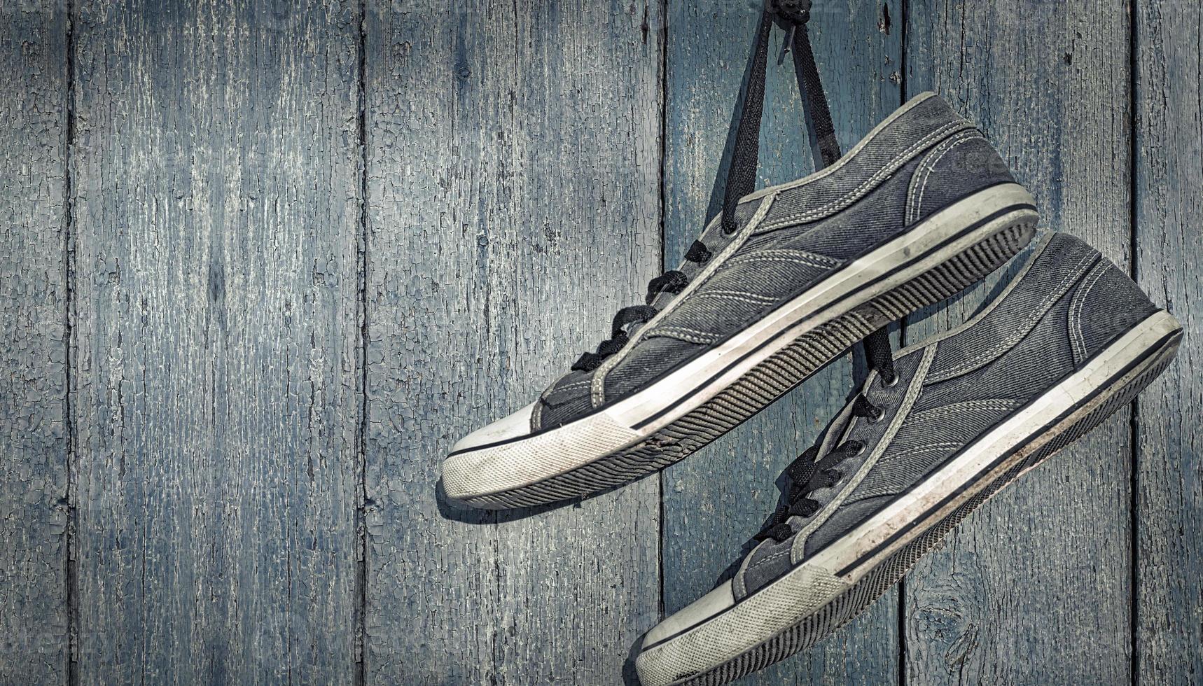 textile torn sneakers hanging from a nail on a background of blue wooden wall photo