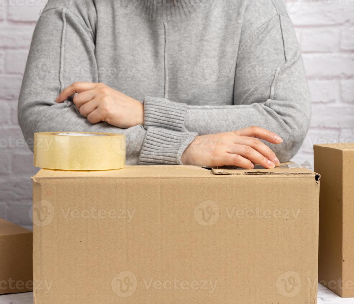 woman in a gray sweater holds a roll of duct tape and packs brown cardboard boxes photo