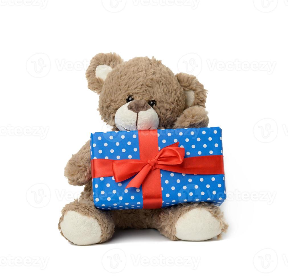 cute brown teddy bear holding a box wrapped in blue paper and red silk ribbon on white isolated background photo