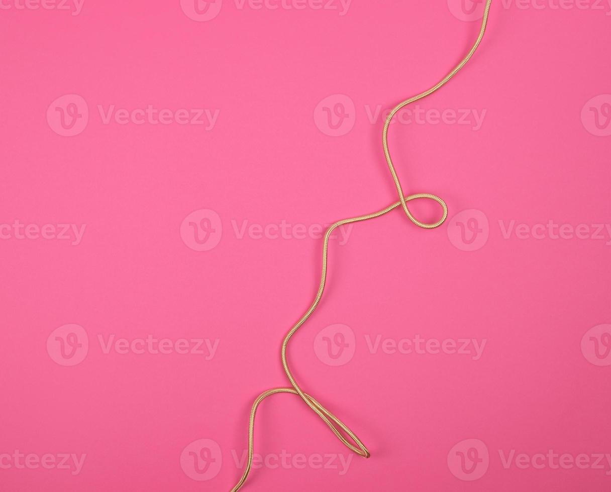 twisted golden cable in a textile winding on a pink background photo