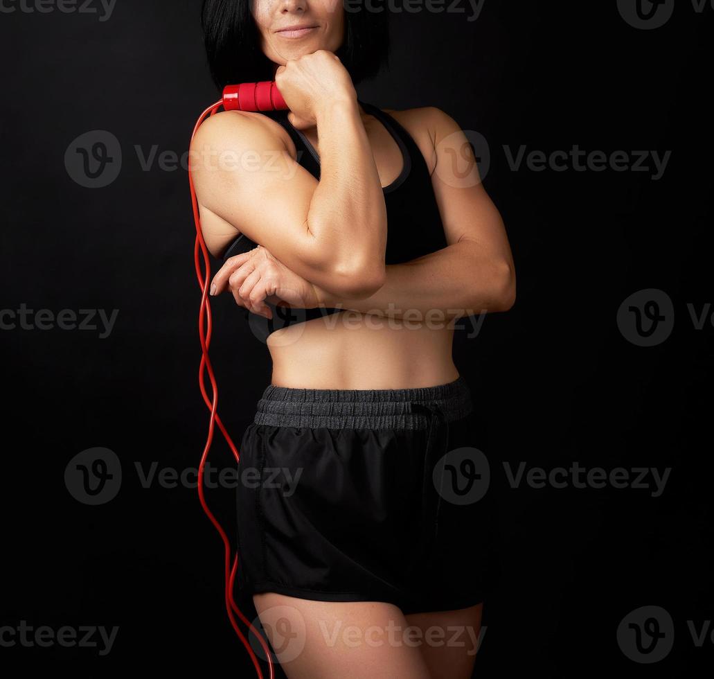 young woman with a sports figure in black uniform holds a red rope for jumping photo