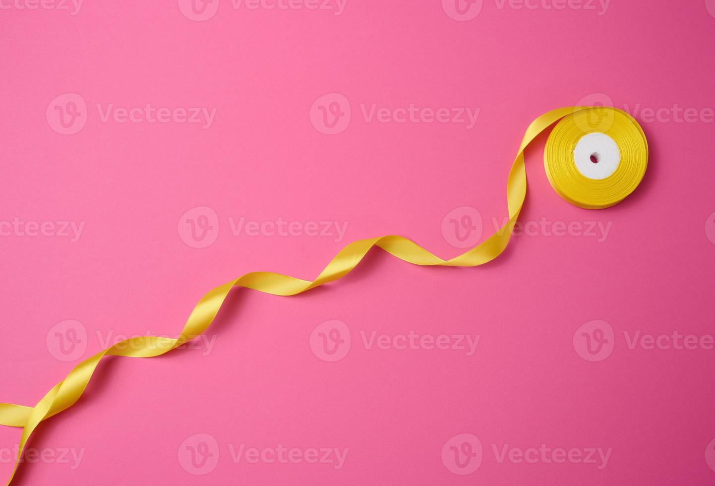 twisted yellow textile ribbon for decoration on a pink background, flat lay photo