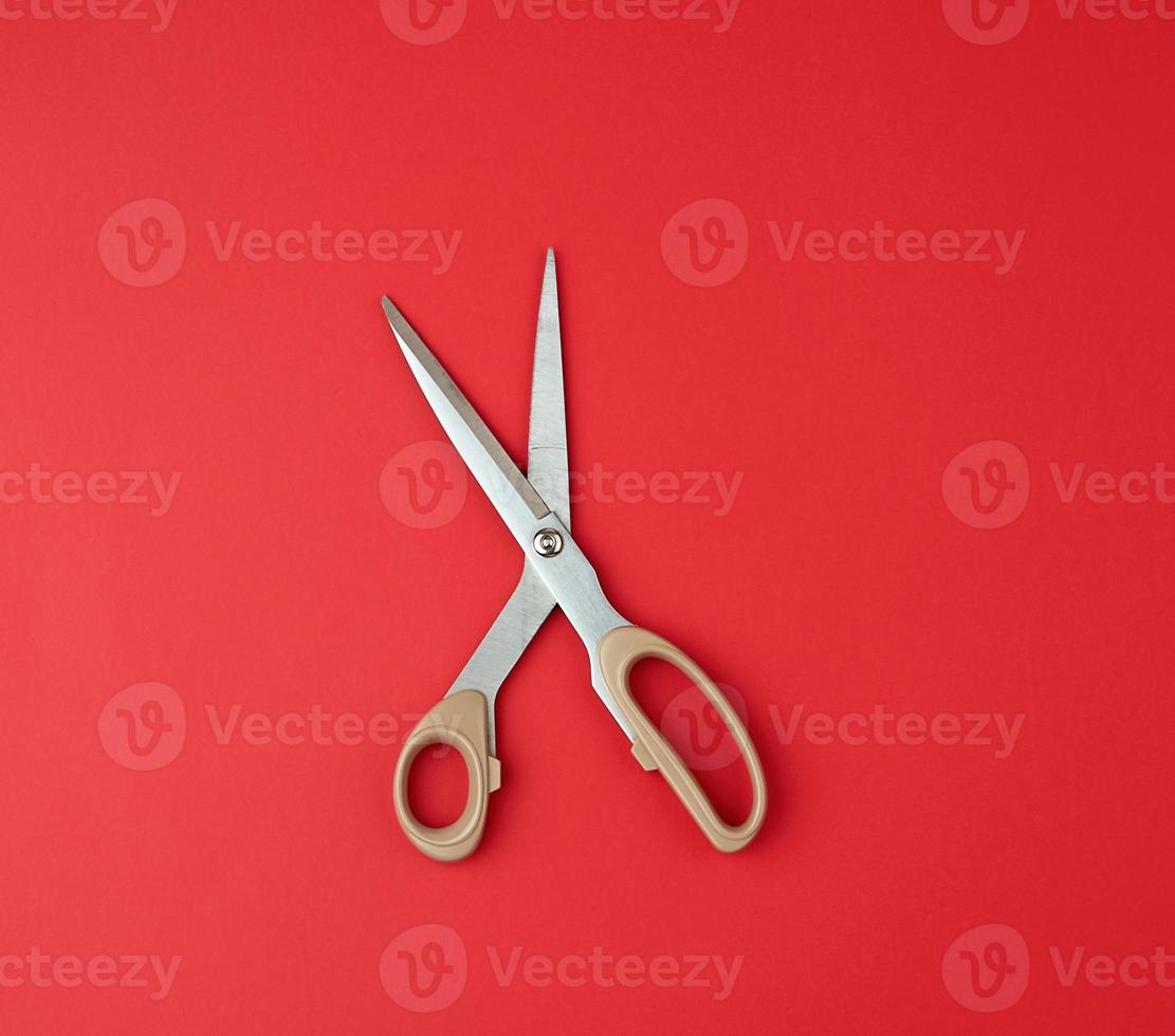 iron scissors with a beige plastic handle on a red background, top view photo