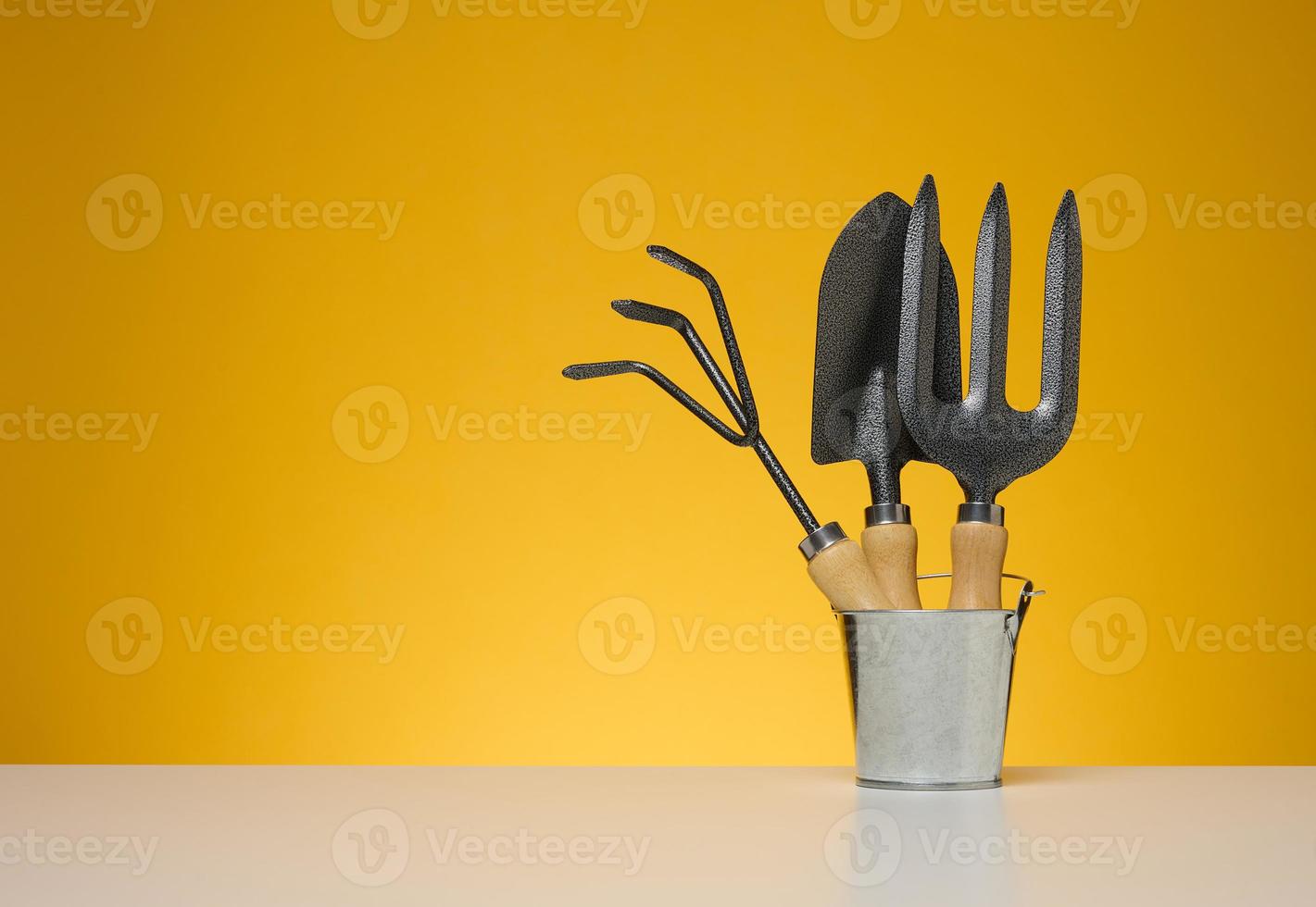 Miniature garden tools in a metal bucket on a yellow background photo