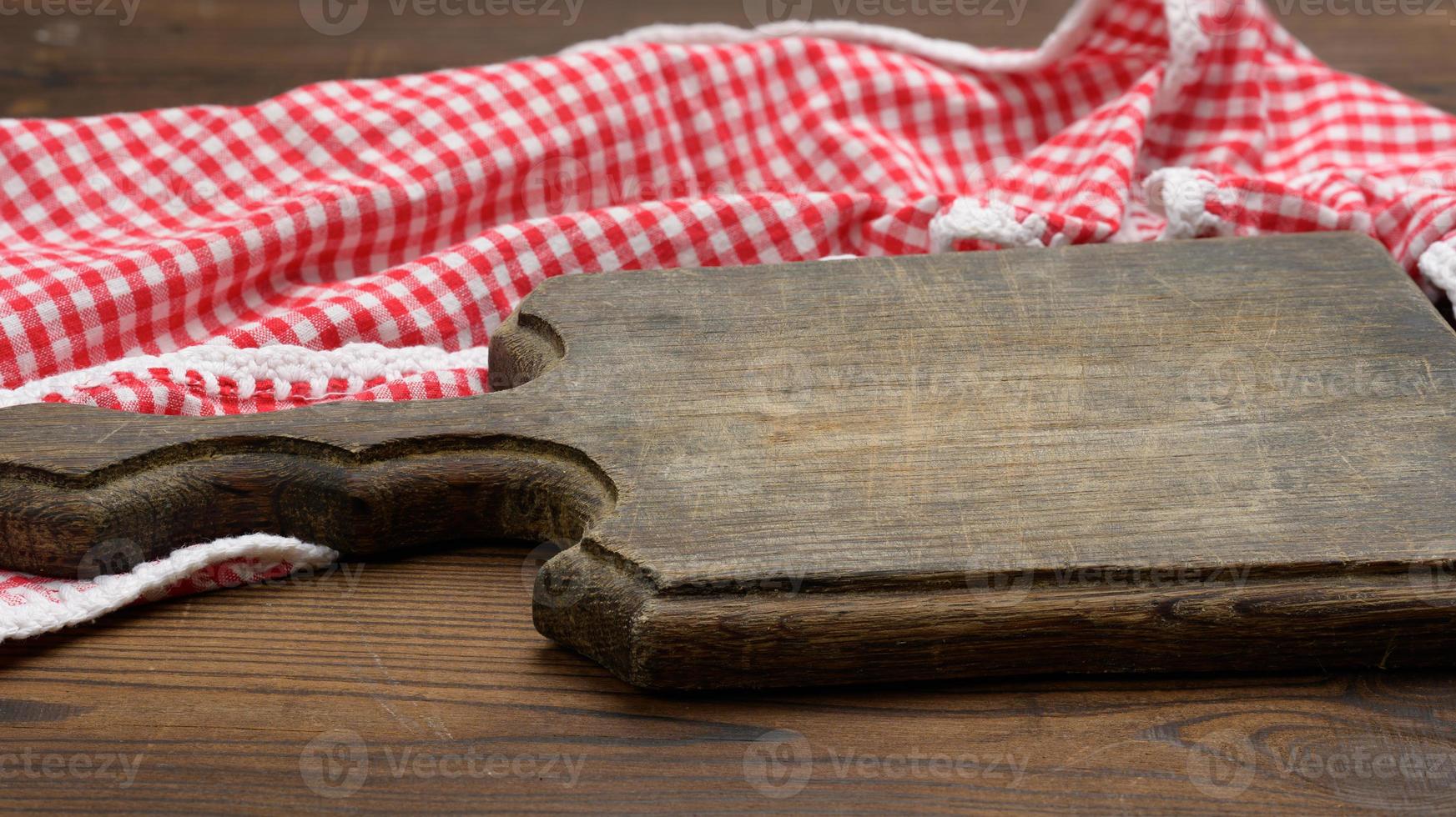 old wooden cutting board and folded red and white cotton kitchen napkin on a wooden brown background, top view, copy space photo