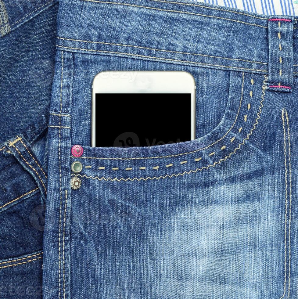 el teléfono inteligente con una pantalla negra en blanco está en el bolsillo delantero de los jeans azules foto