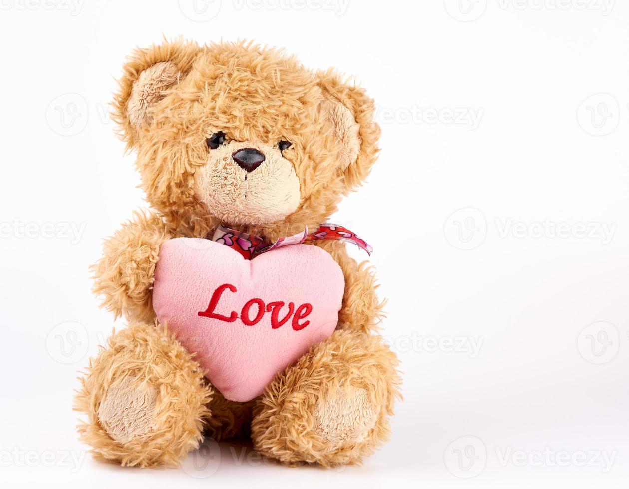 beige teddy bear holds a pink heart, white background photo