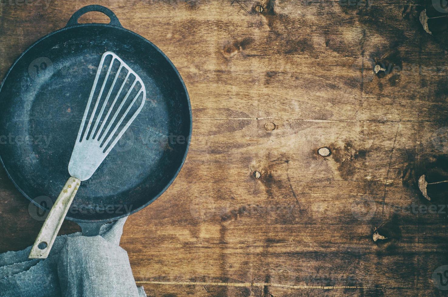 Black empty frying pan with an iron spatula on a brown wooden surface photo