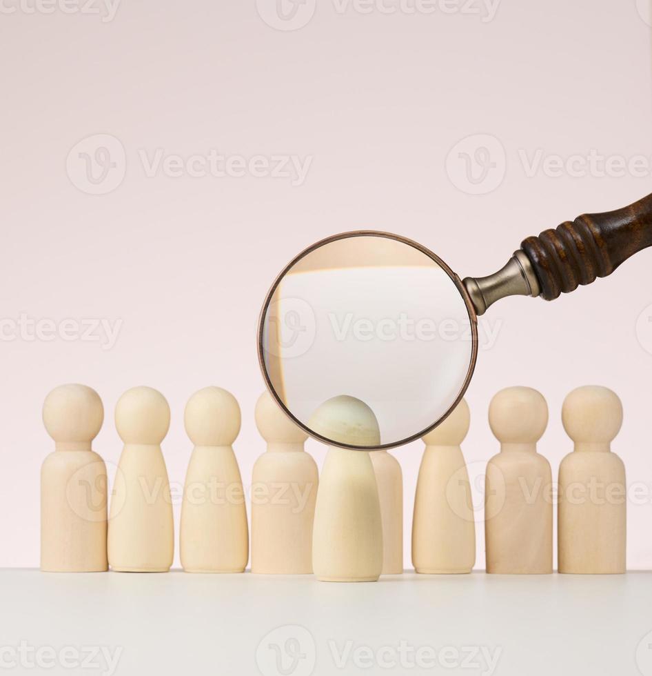 wooden figures of men stand on a beige background and a wooden magnifying glass. Recruitment concept, search for talented and capable employees, career growth photo
