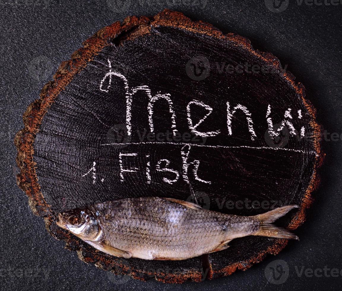 Dried fish carp on a black wooden cut tree photo