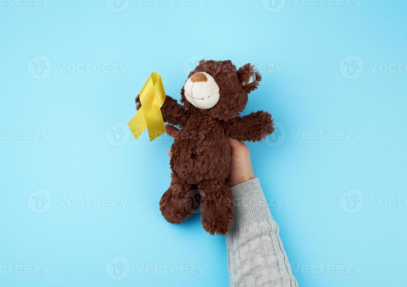small brown teddy bear which holds in its paw a yellow ribbon folded in a loop photo