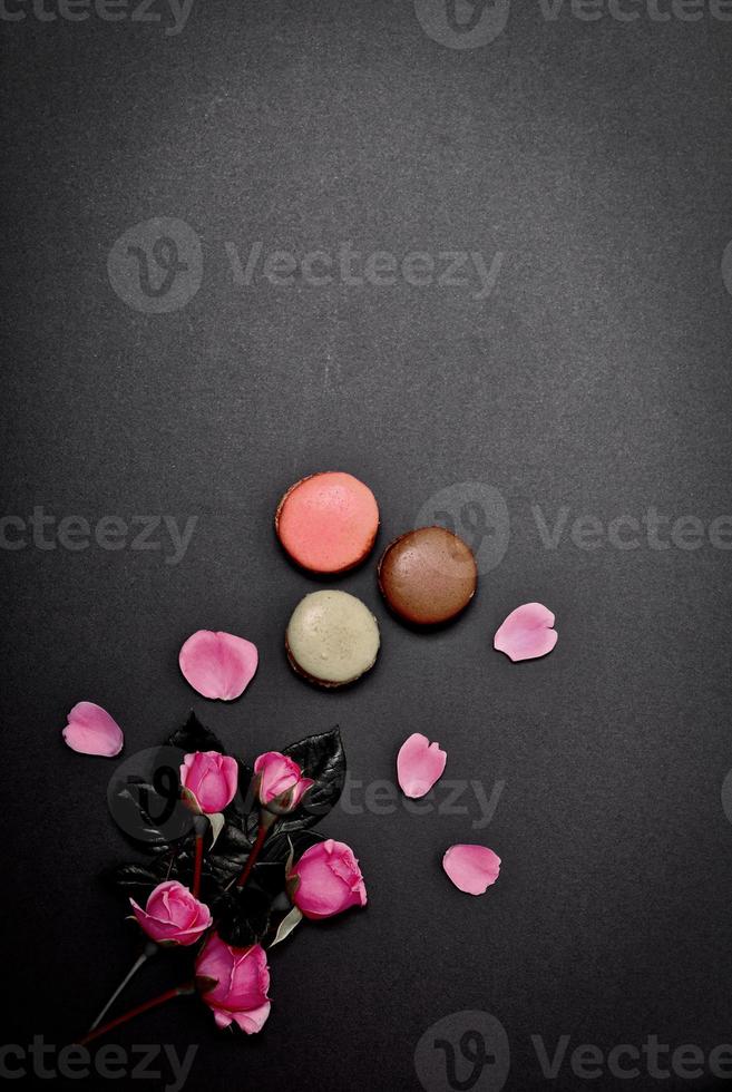 black background with macaroons and a bouquet of pink roses photo