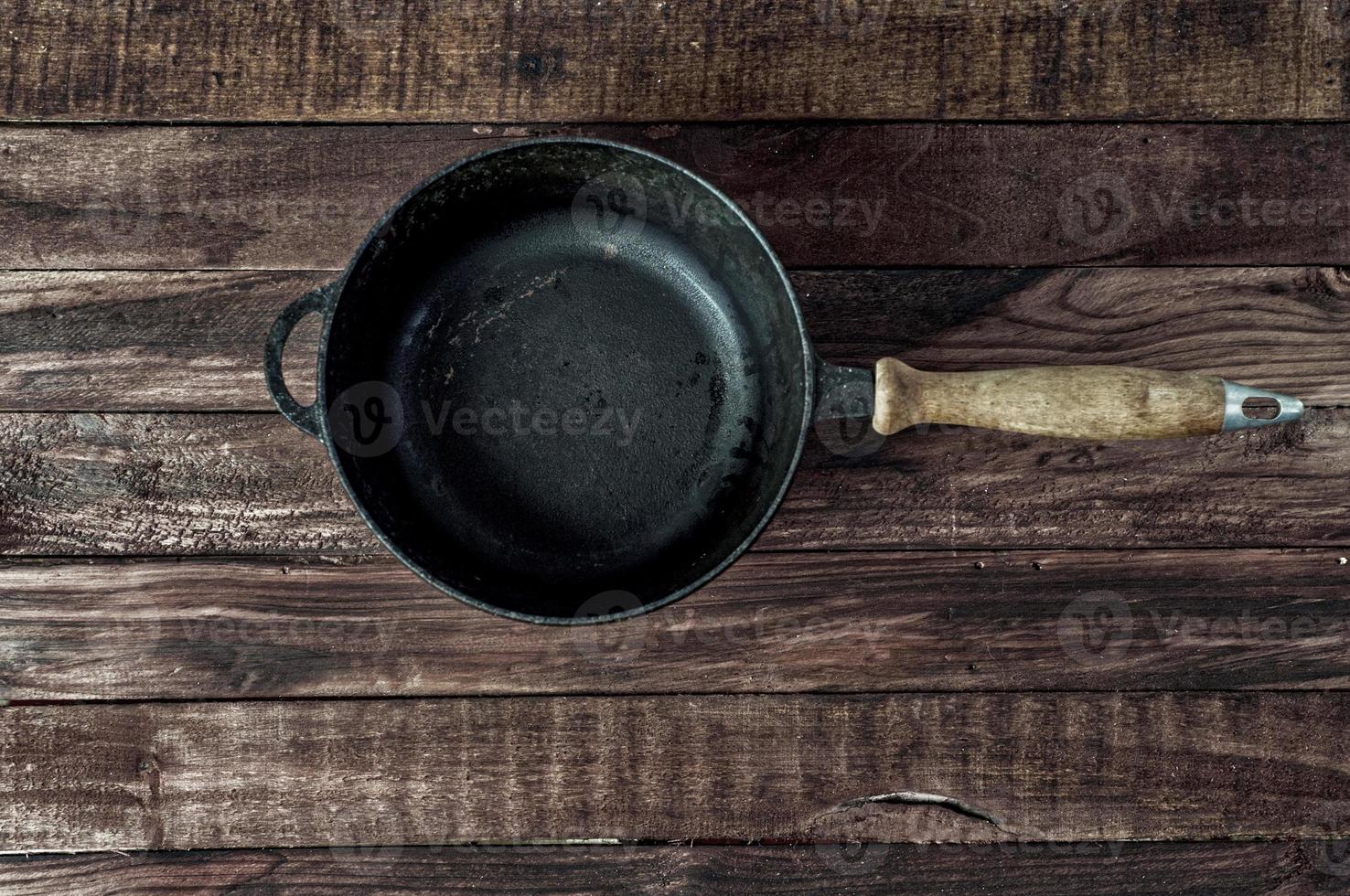 Black cast-iron frying pan on a brown wooden surface photo