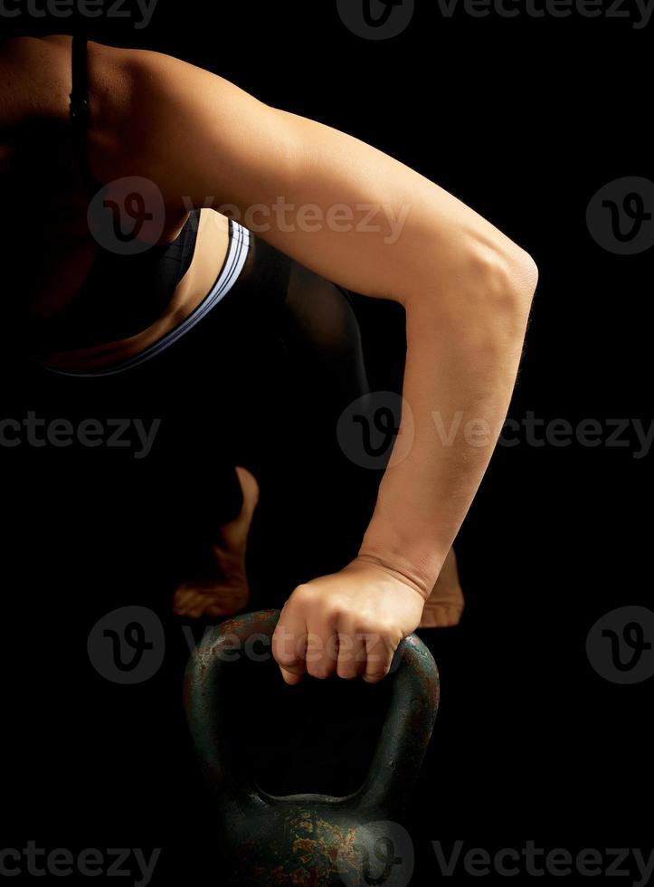 young girl of athletic appearance with black hair is pushing up from an iron kettlebell photo