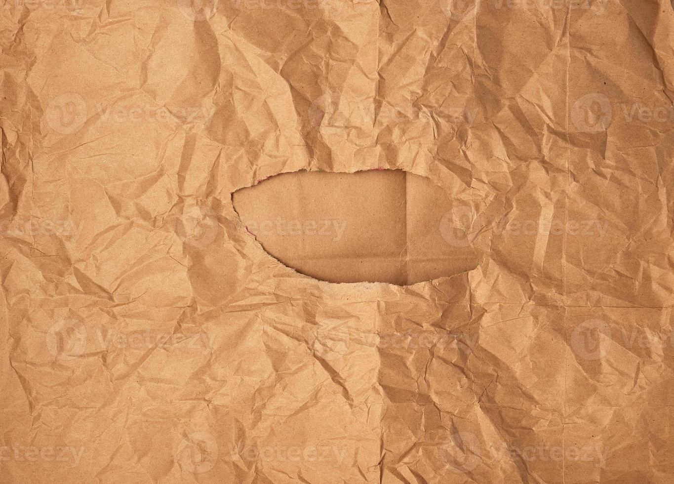 crumpled brown sheet of paper with a hole, in the middle of a brown background photo