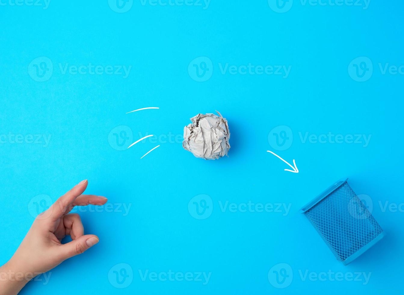 hand pushed a ball of crumpled gray paper into a metal wastebasket photo