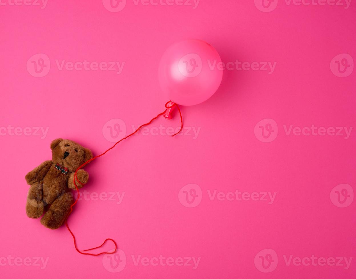 little brown teddy bear holding a pink inflated balloon on a rope photo