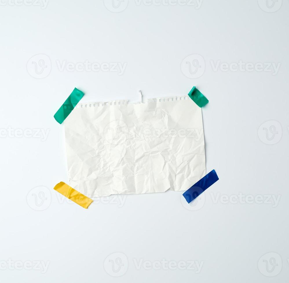 white crumpled sheet of paper torn from a spiral notebook and glued with multi-colored electrical tape on a white background photo