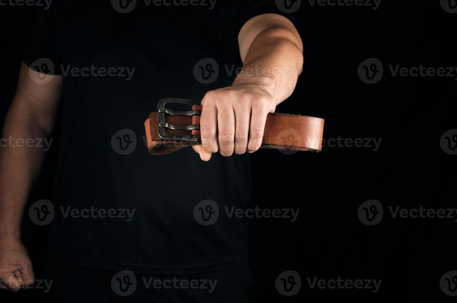 man in black clothes is holding a brown leather belt with a buckle photo