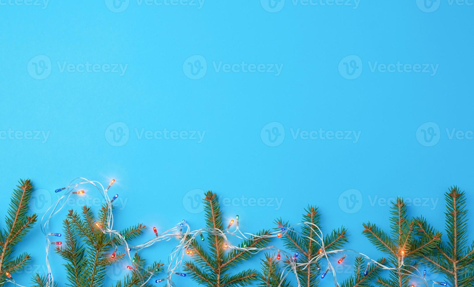 burning multi-colored light bulbs on a garland with a white cable and green twigs of needles photo