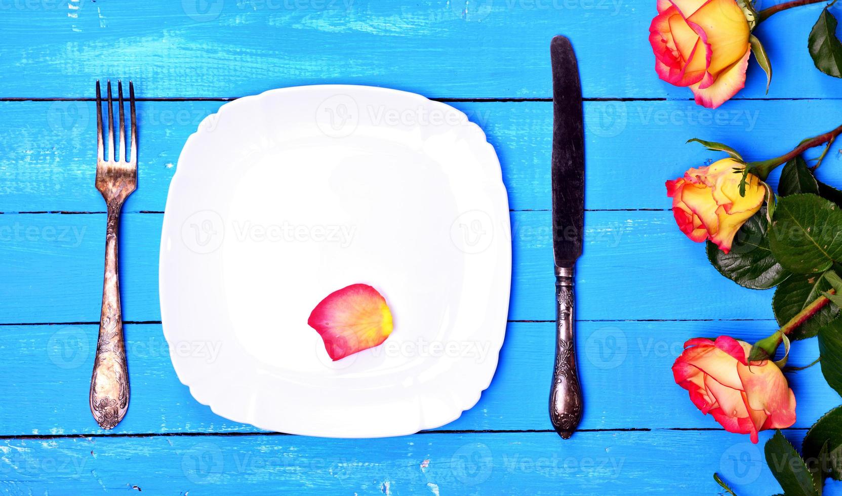 White plate with knife and fork on a blue wooden background photo