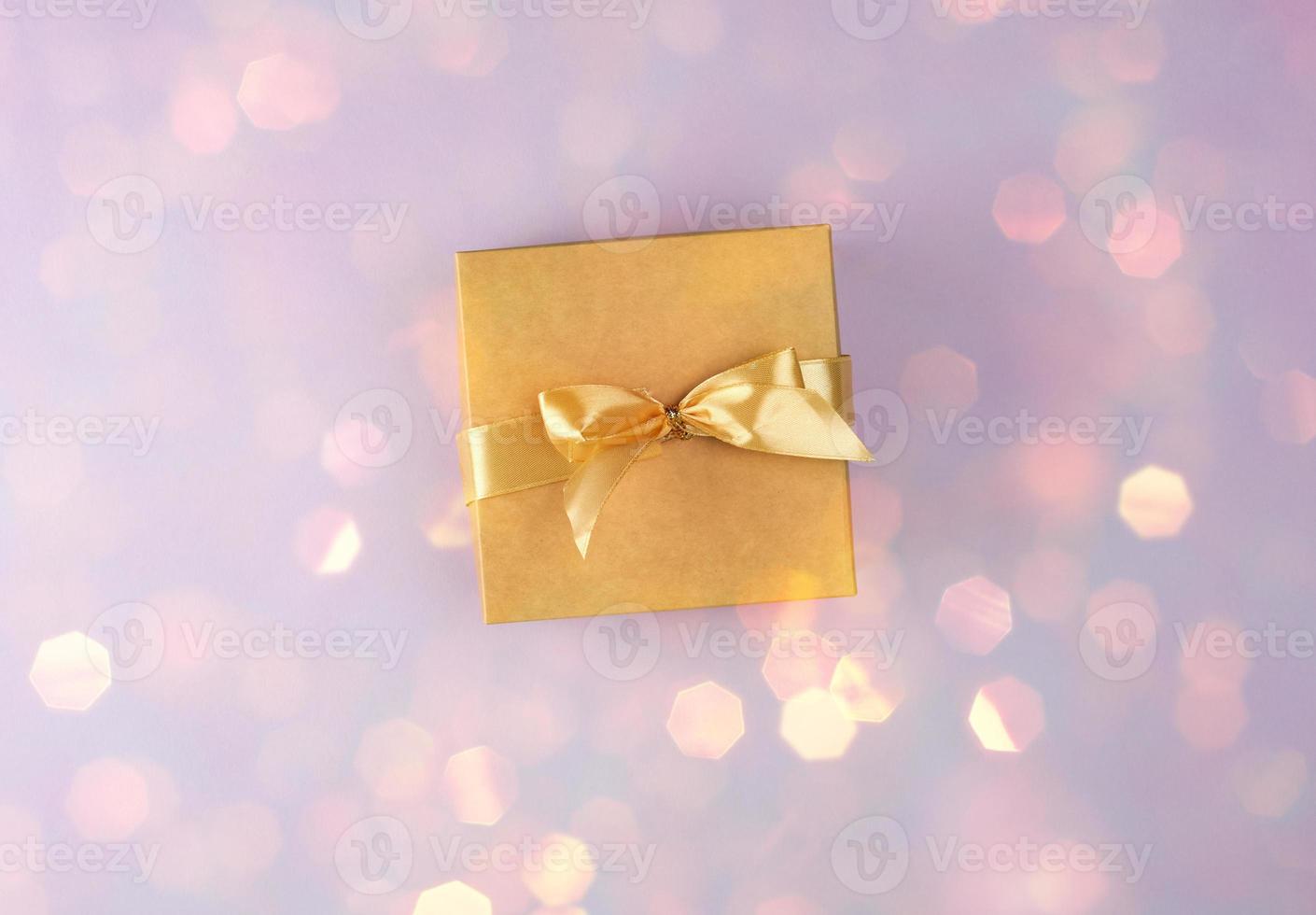 brown paper box with bow on purple background with shiny yellow bokeh photo