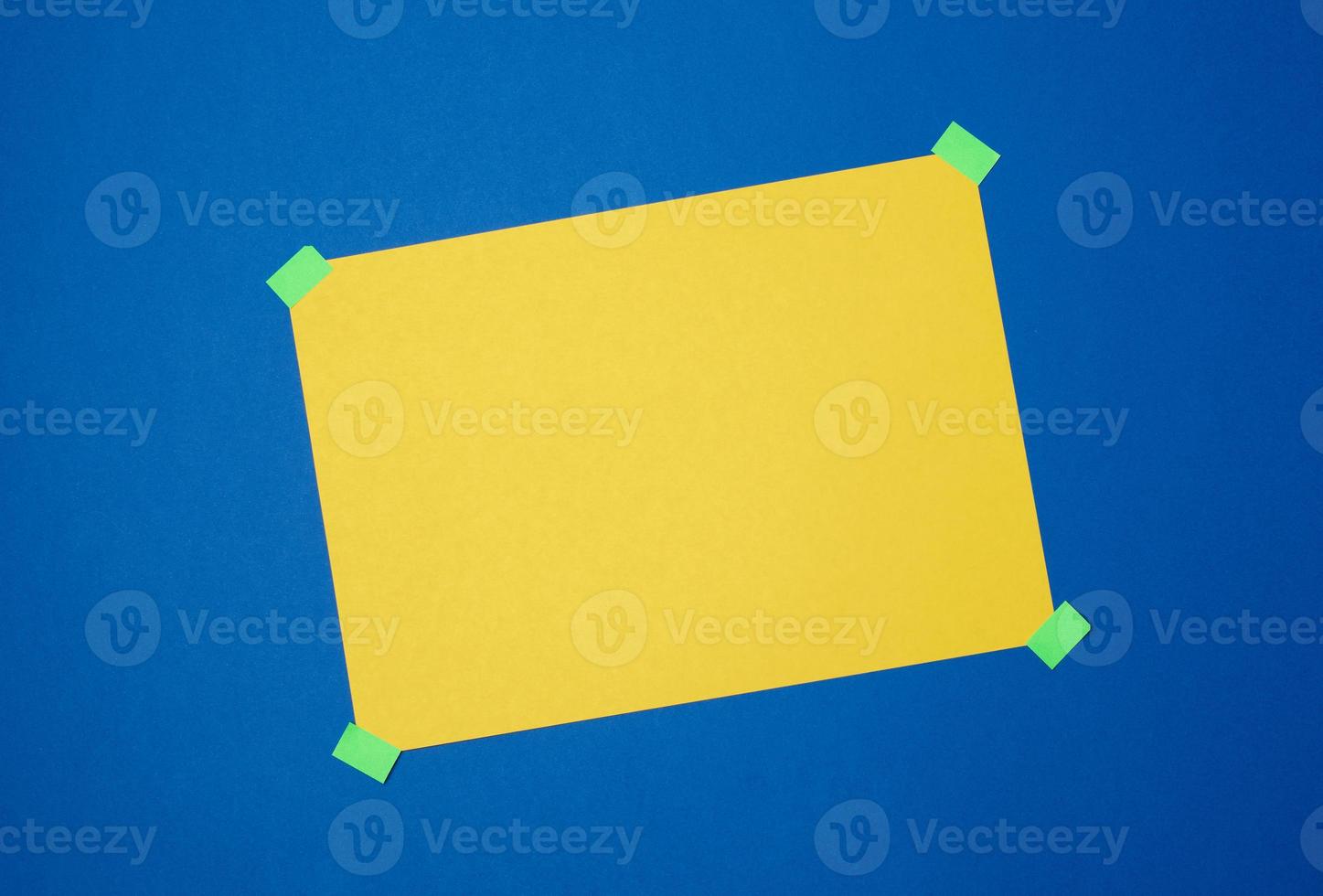 blank yellow sheet of paper stuck with green sticky tape on a blue background photo