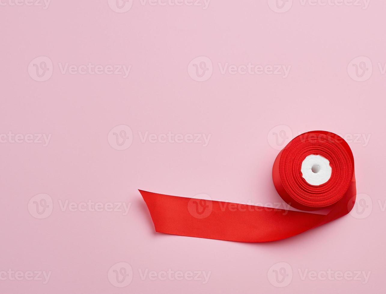 spools with red satin ribbon on a pink background photo