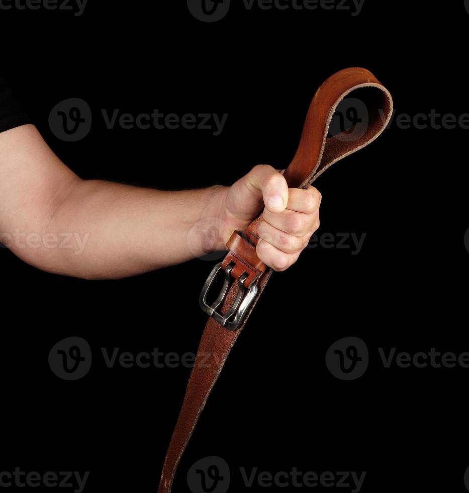 brown leather belt with an iron buckle in a man's hand, black background photo