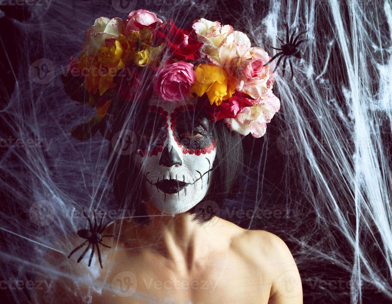 la chica con el pelo negro está vestida con una corona de rosas multicolores y el maquillaje está hecho en su cara calavera de azúcar hasta el día de los muertos foto
