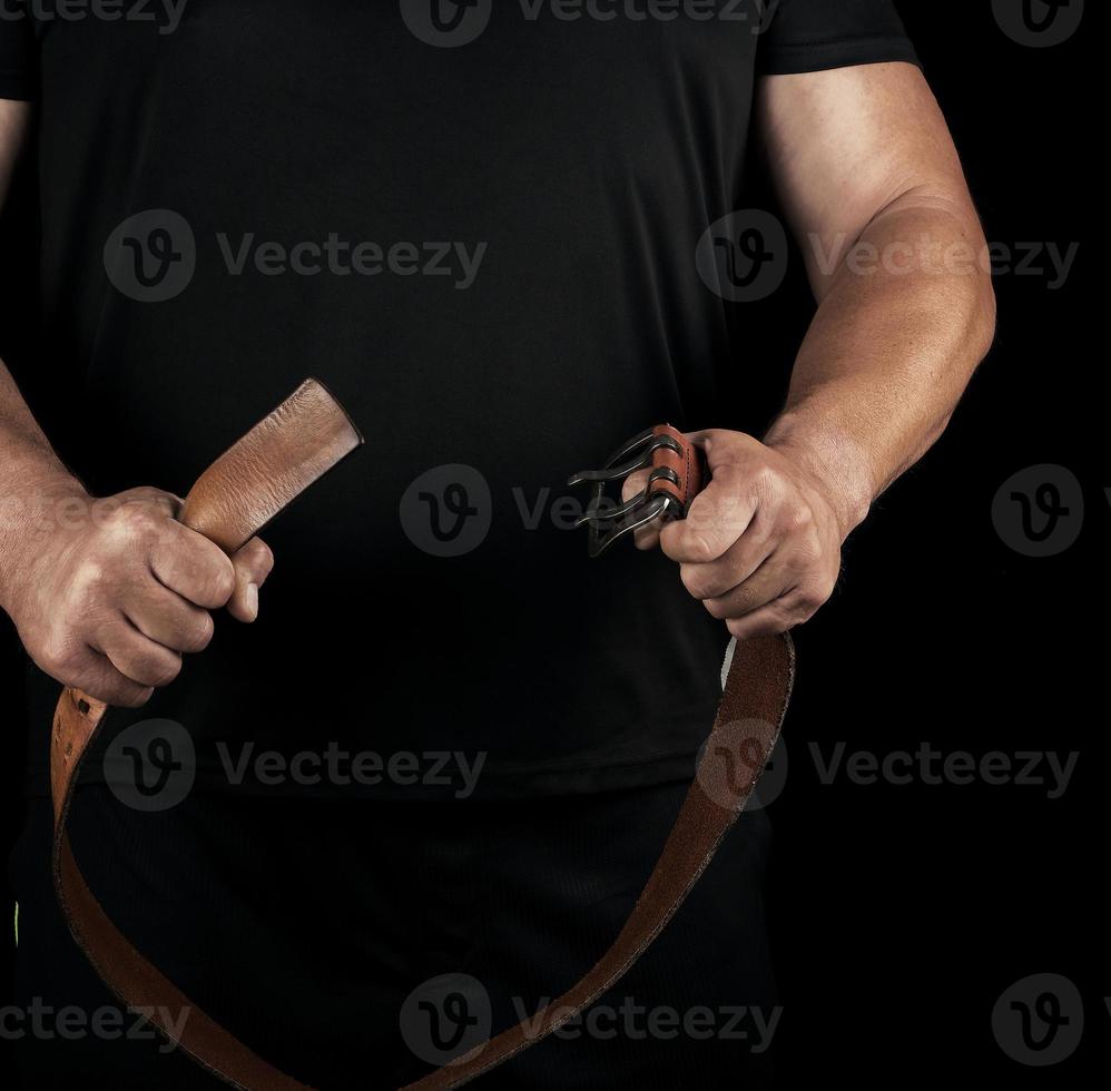 adult man in black clothes holding a brown leather belt with an iron buckle photo