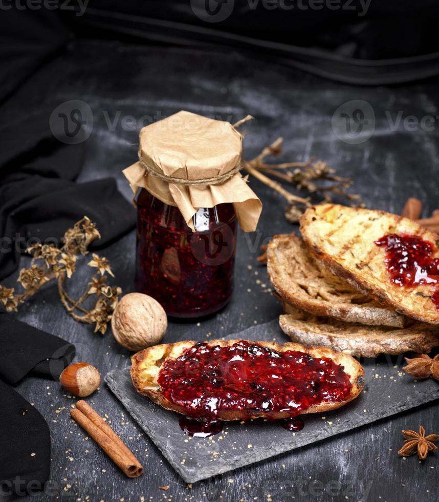 toast of white bread with raspberry jam and a glass jar with jam photo
