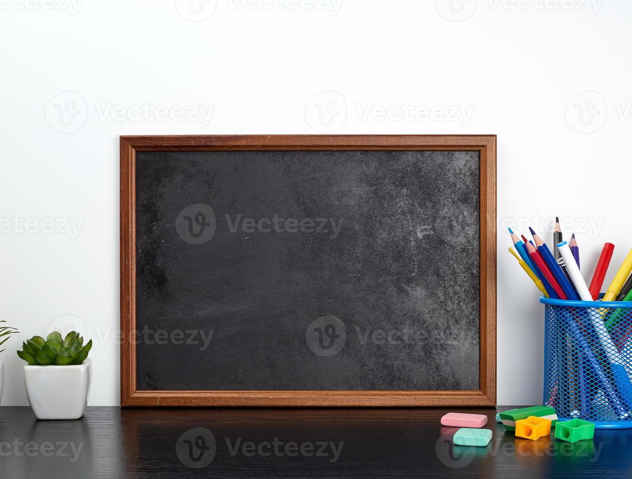 empty black chalk board, multi-colored pencils in a blue metal stand on a black table photo