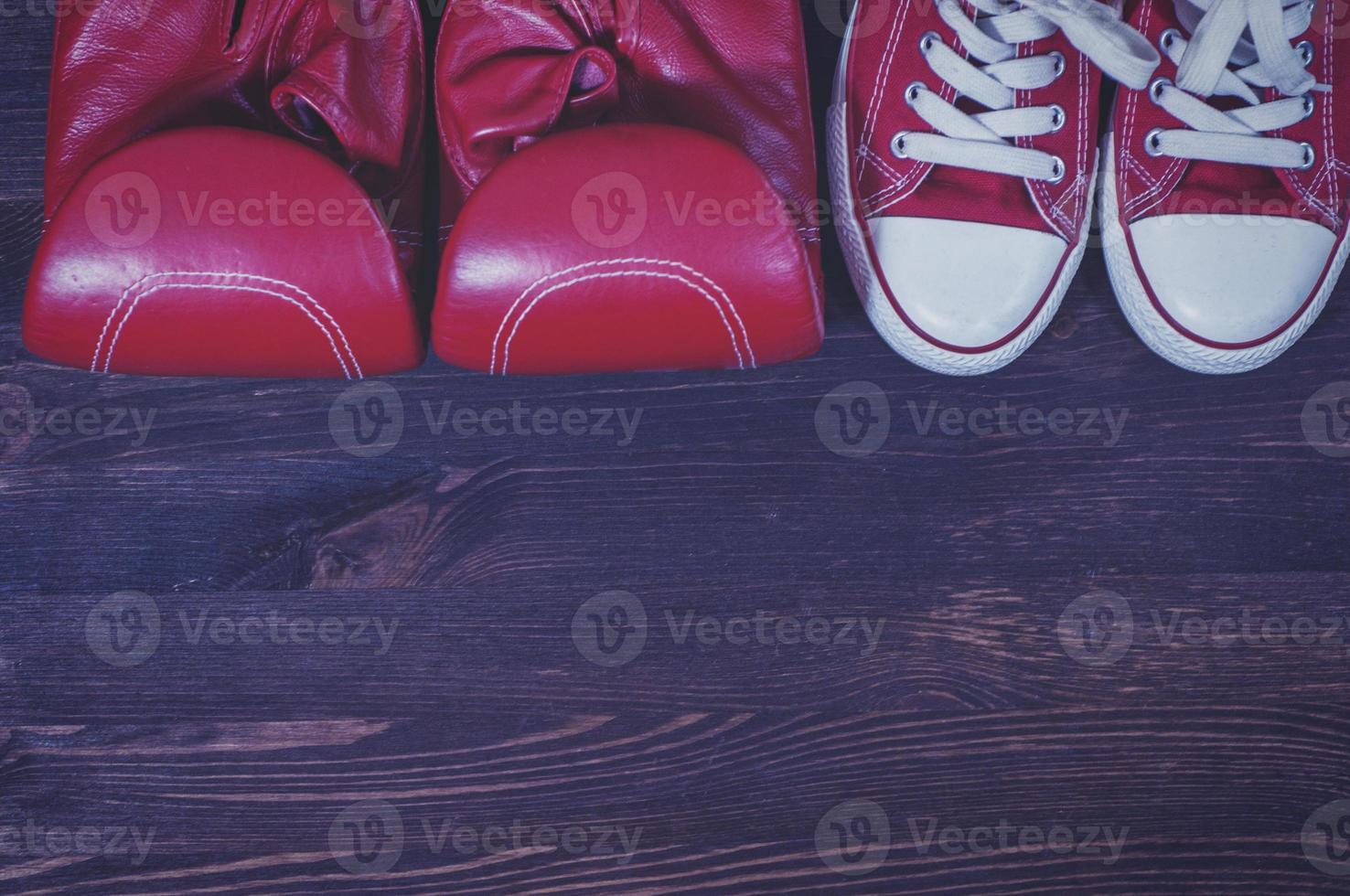 Red boxing gloves and a pair of red sneakers on a brown wooden surface photo