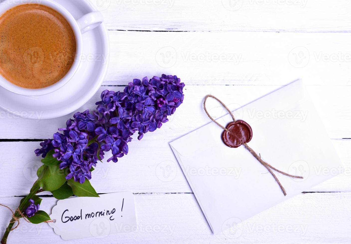 sealed letter on a white wooden surface, near a lilac bud and a cup of espresso photo