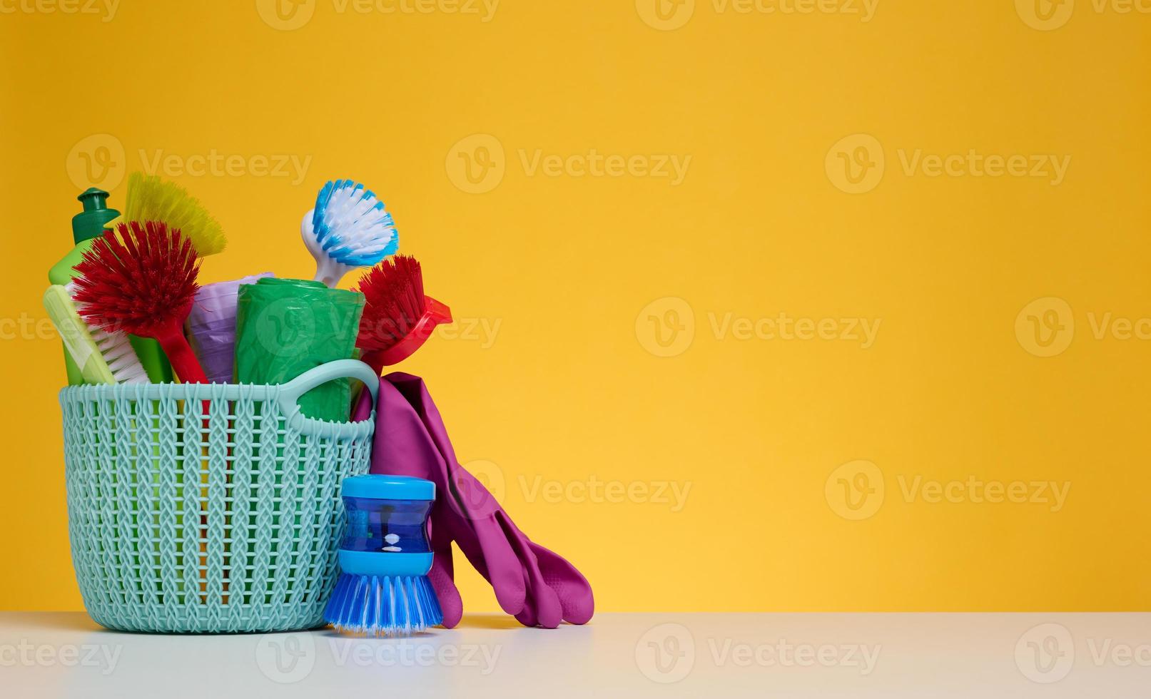 Plastic basket with brushes, disinfectant in a bottle, rubber gloves on a yellow background photo