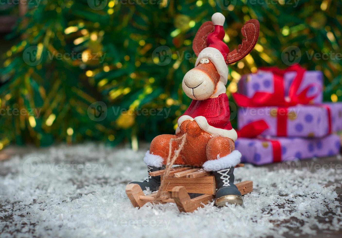 Christmas toy deer in holiday clothes on wooden sleigh among snow photo