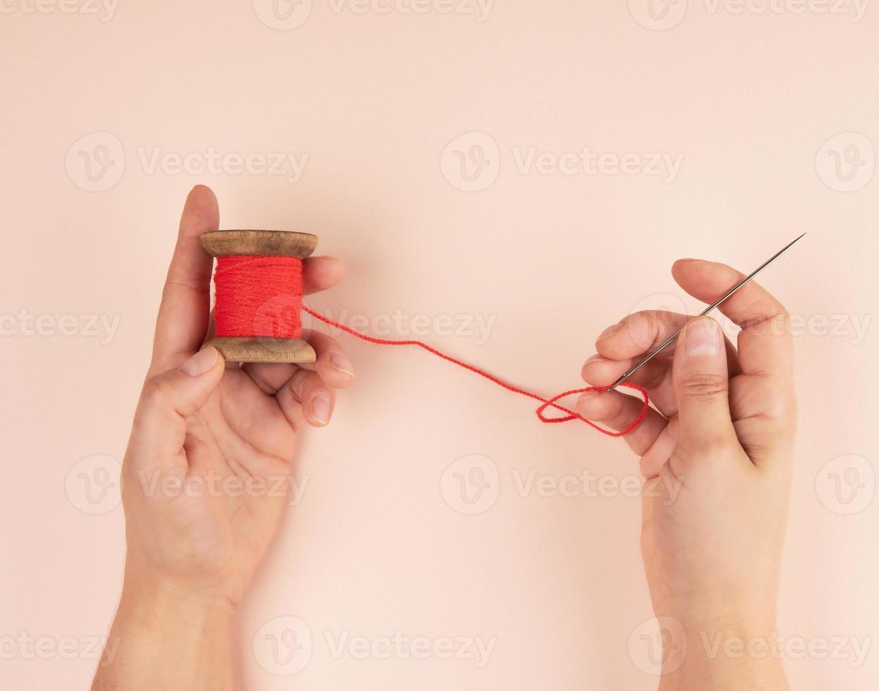 two hands hold a wooden bobbin with red wool threads photo