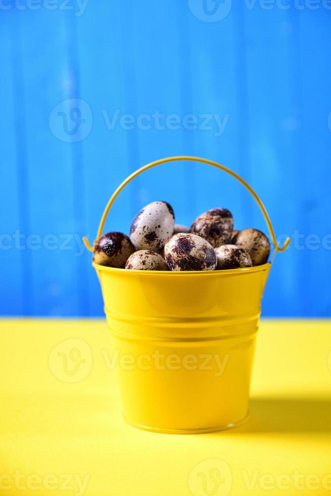 Full bucket of fresh quail eggs in the shell on a yellow surface photo