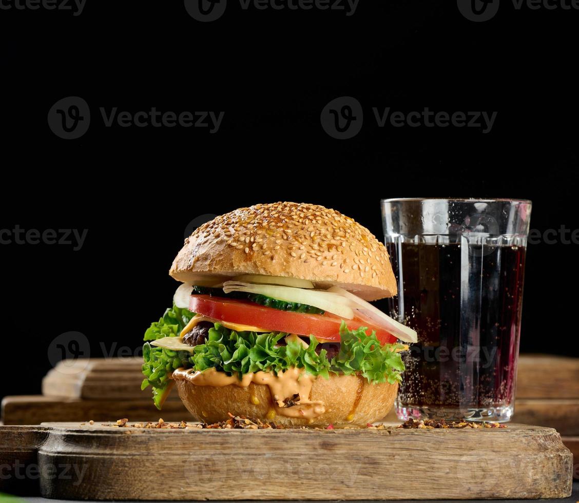 cheeseburger with grilled beef patty, cheddar cheese, tomato and lettuce on a wooden board, black background photo