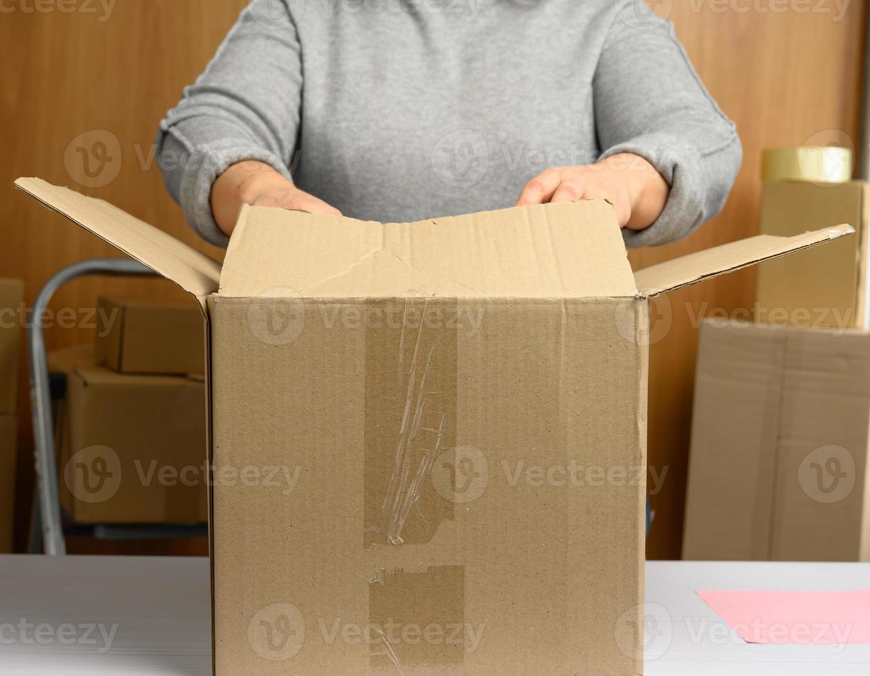 woman in a gray sweater is packing brown cardboard boxes on a white table photo