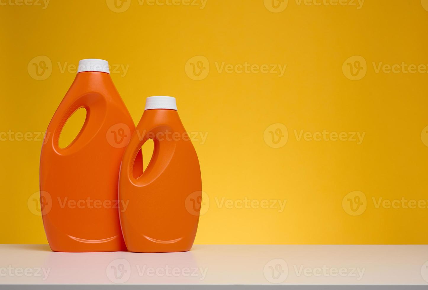 dos botellas de plástico naranja con detergente líquido sobre una mesa blanca, fondo amarillo foto