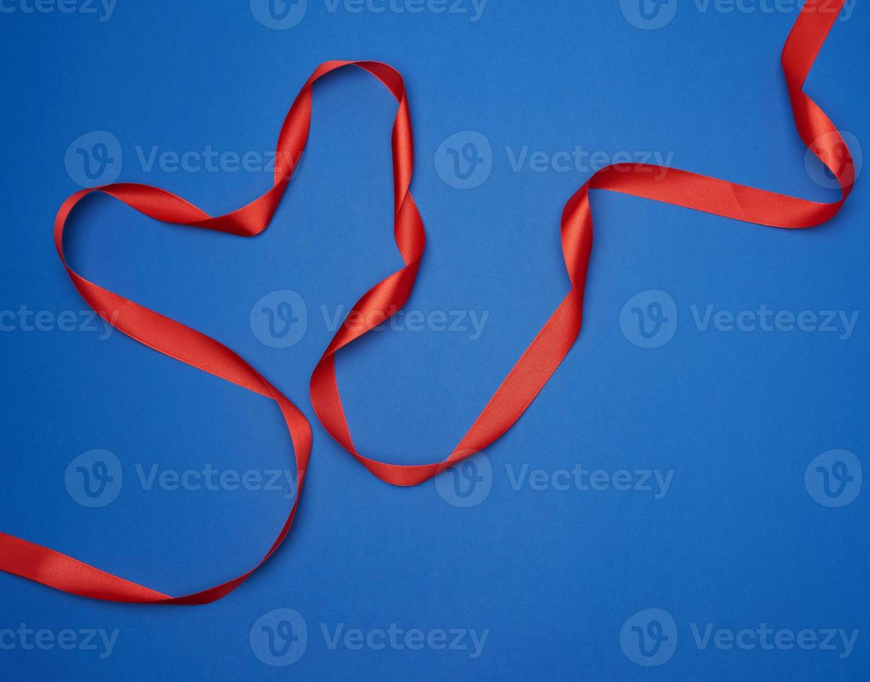 red silk thin ribbon twisted on a blue background photo