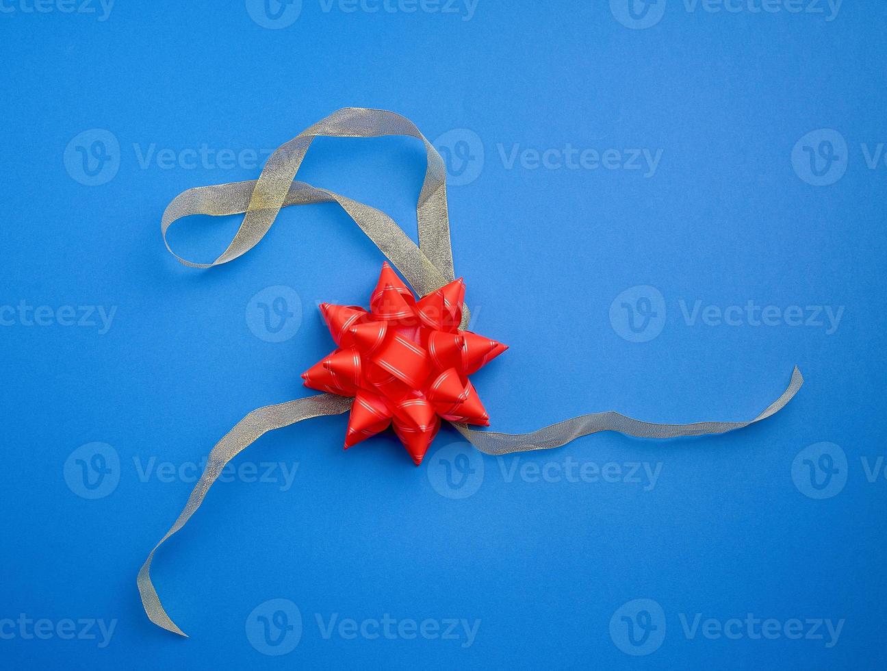 golden silk thin ribbon twisted and red shiny bow on a blue background photo