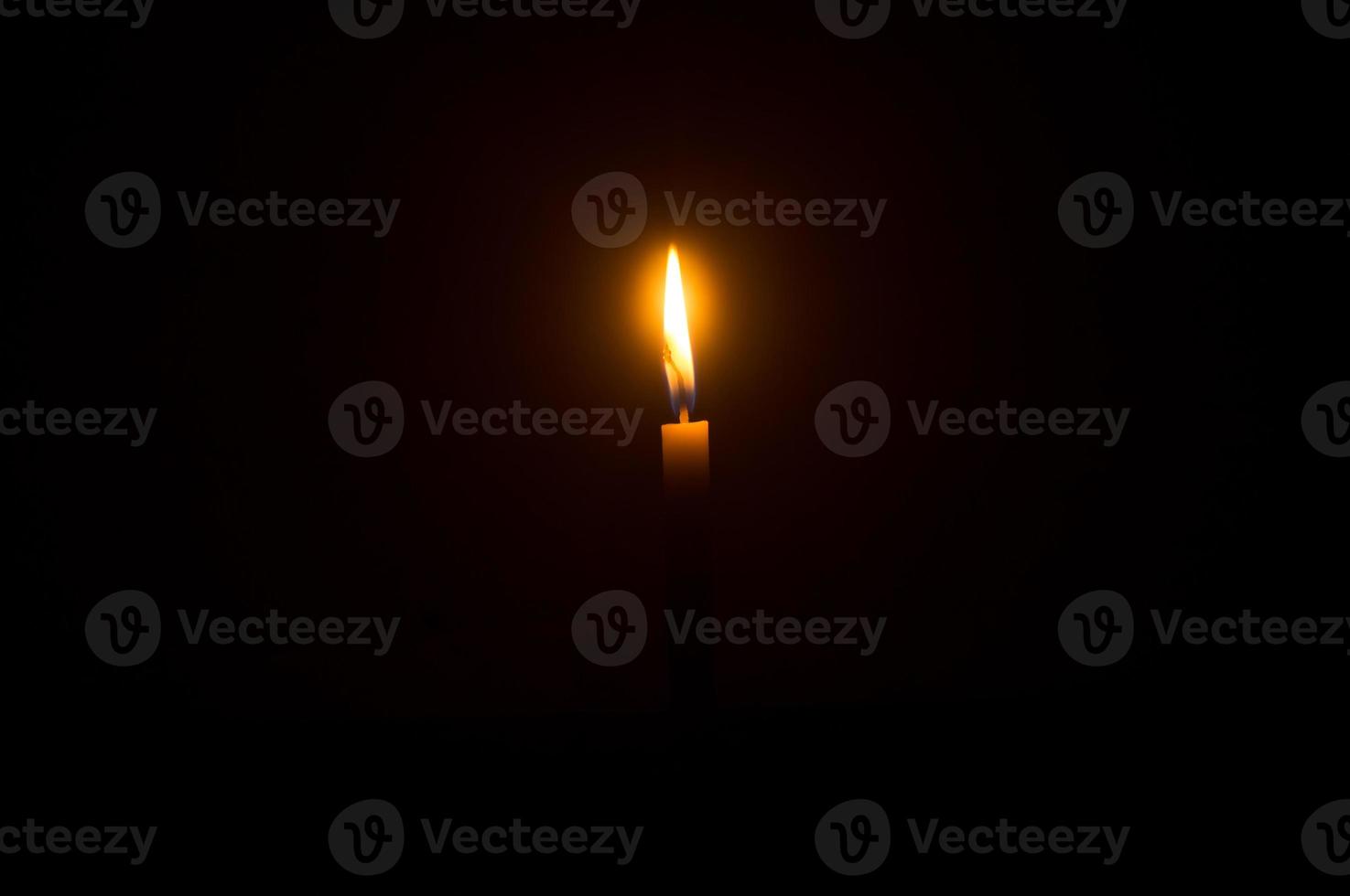 Single burning candle flame or light glowing on an orange candle on black or dark background on table in church for Christmas, funeral or memorial service photo
