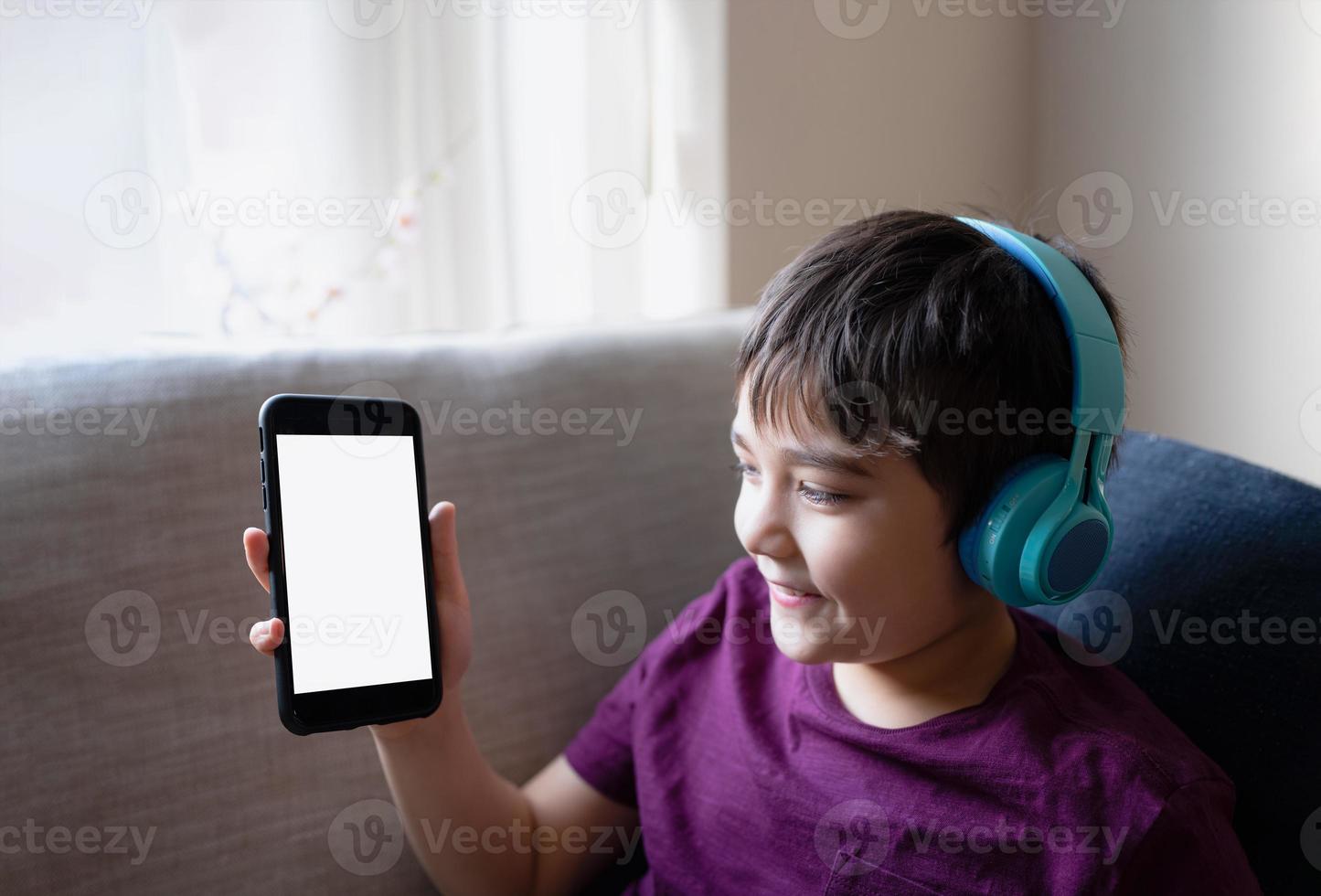 niño que muestra la pantalla móvil y usa el teléfono móvil para buscar información en Internet para la tarea, niño que usa auriculares para escuchar música, educación en el hogar, educación de aprendizaje electrónico, niños con tecnología foto