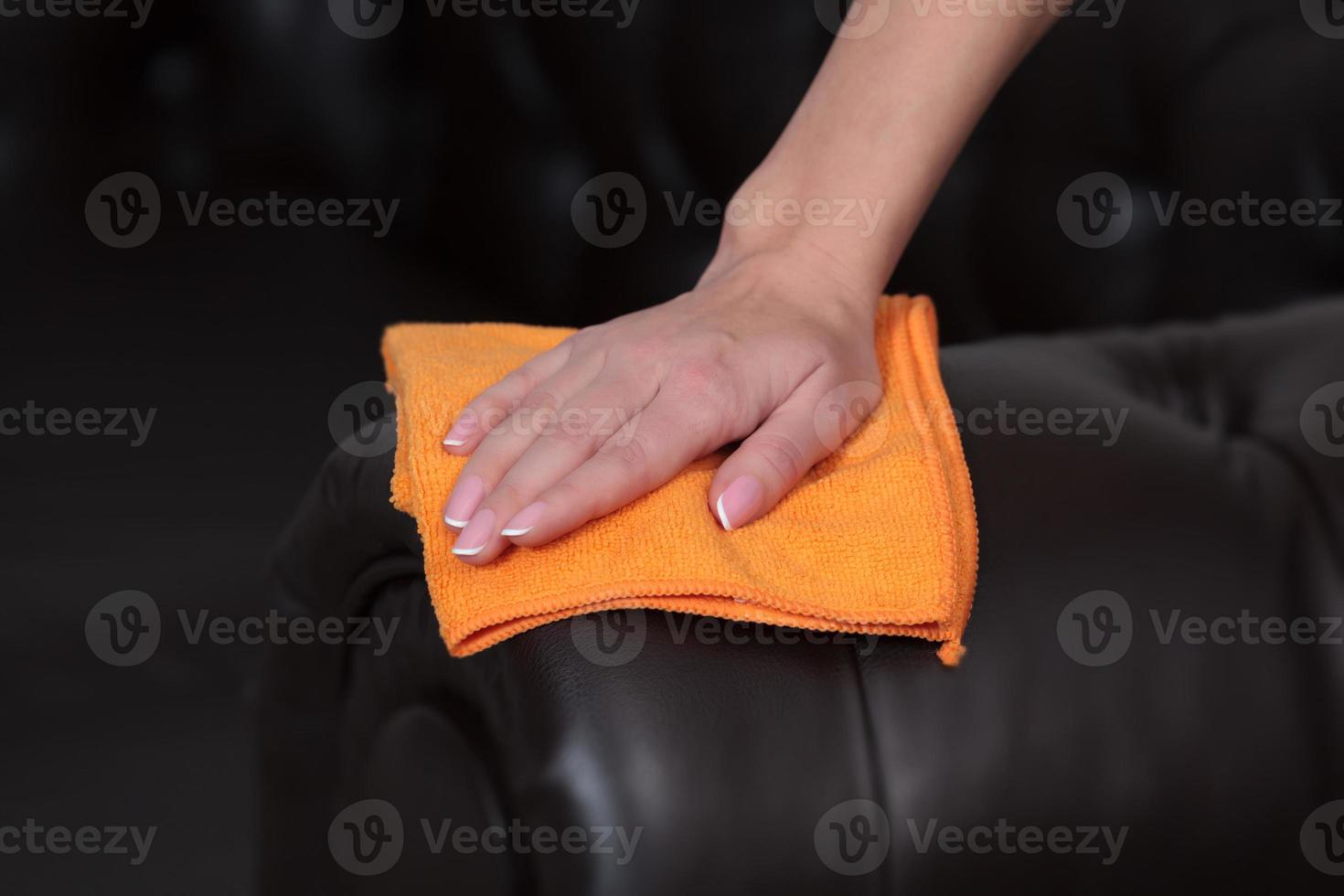 Closeup shot of female hand wiping brown leather chester couch of sofa photo