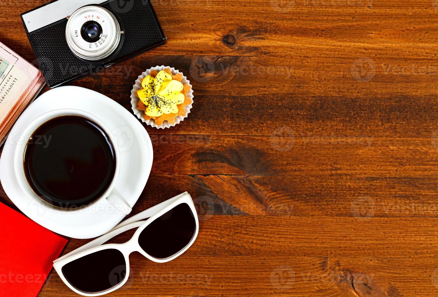 cámara de fotos retro, taza de café, pasaporte, gafas de sol y quequitos en una mesa de madera marrón con espacio para texto, vista superior.