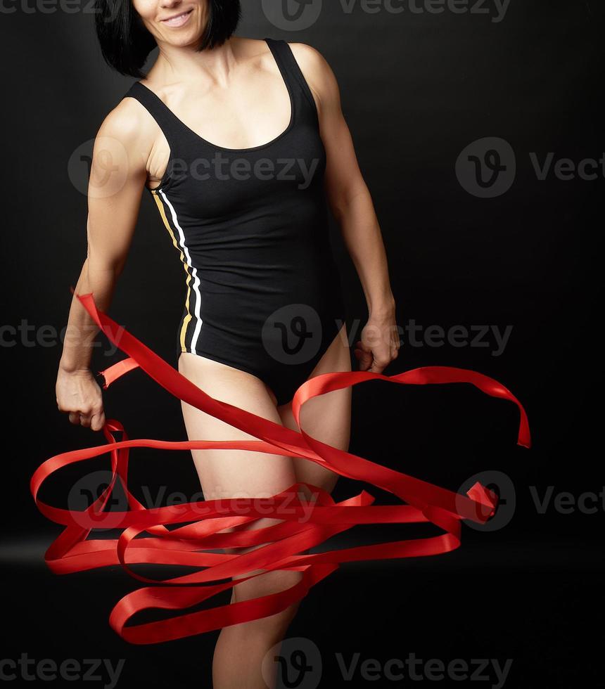 young woman gymnast of Caucasian appearance with black hair spins red satin ribbons, gymnastic exercises photo